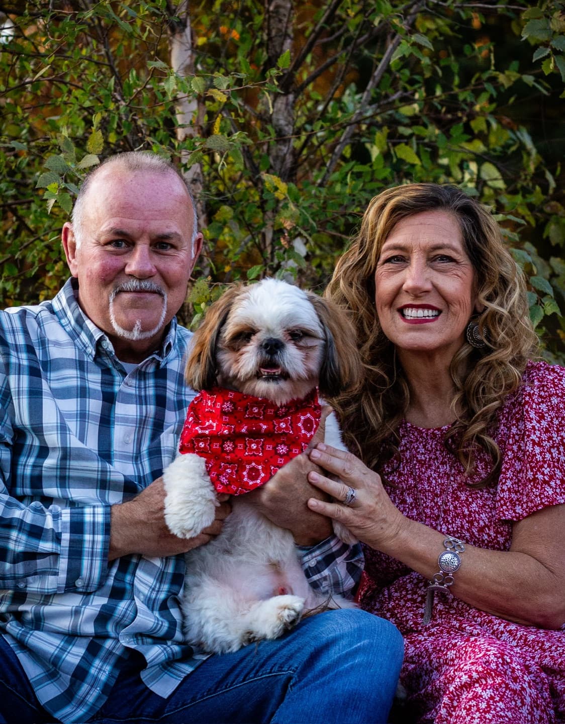 A couple sitting close with their little dog in a red bandana