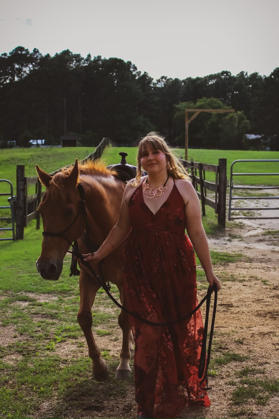 A young woman in a red dress leading her horse across the pasture