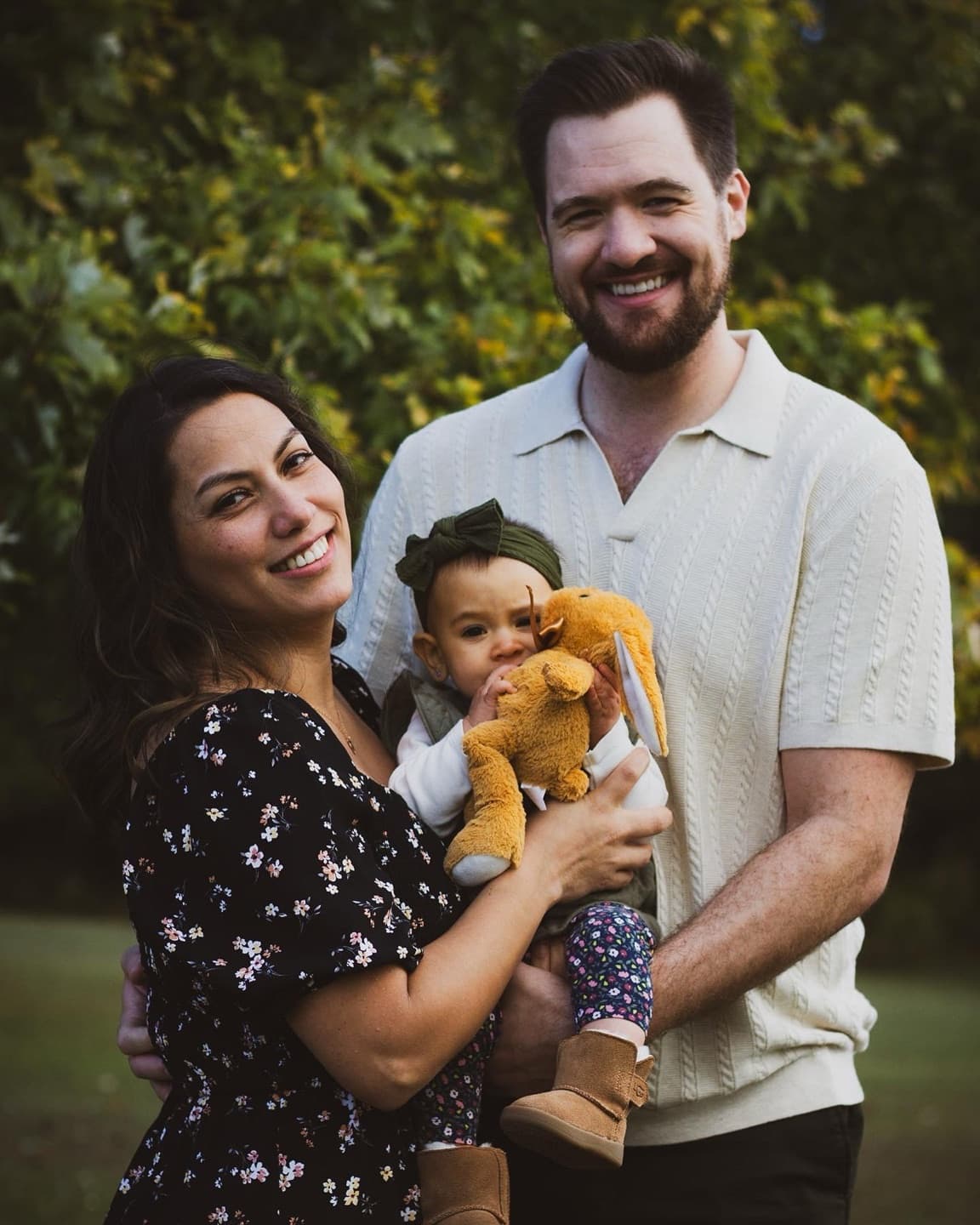 A mother and father holding their baby, who clutches a stuffed animal