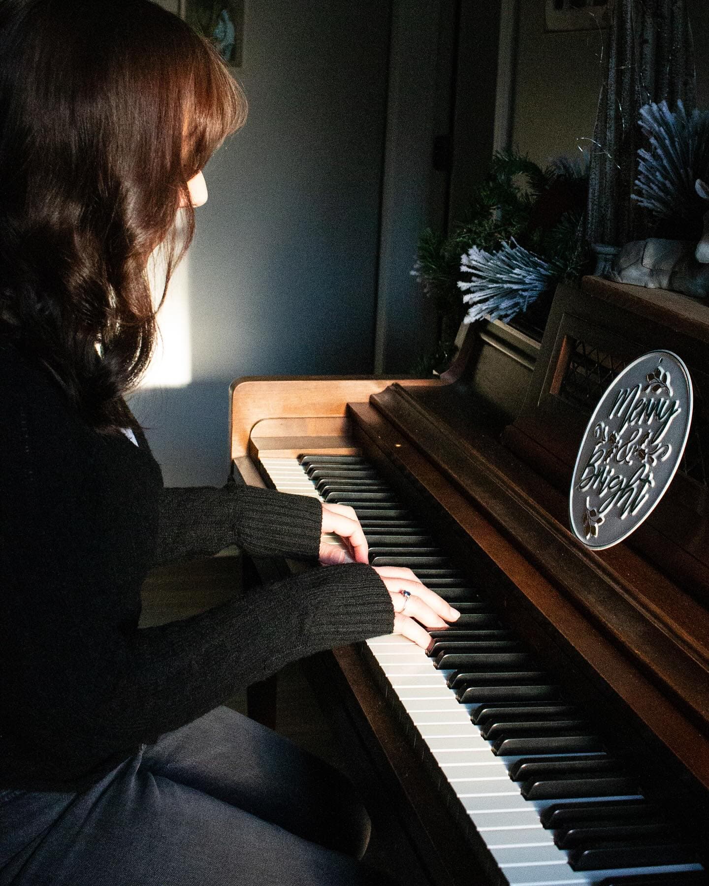 A girl seated at an upright piano in warm afternoon light