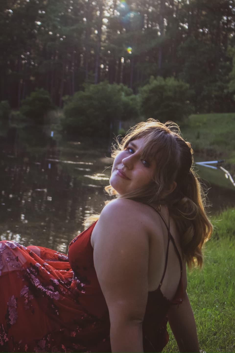 A young woman looking over her shoulder beside a quiet pond