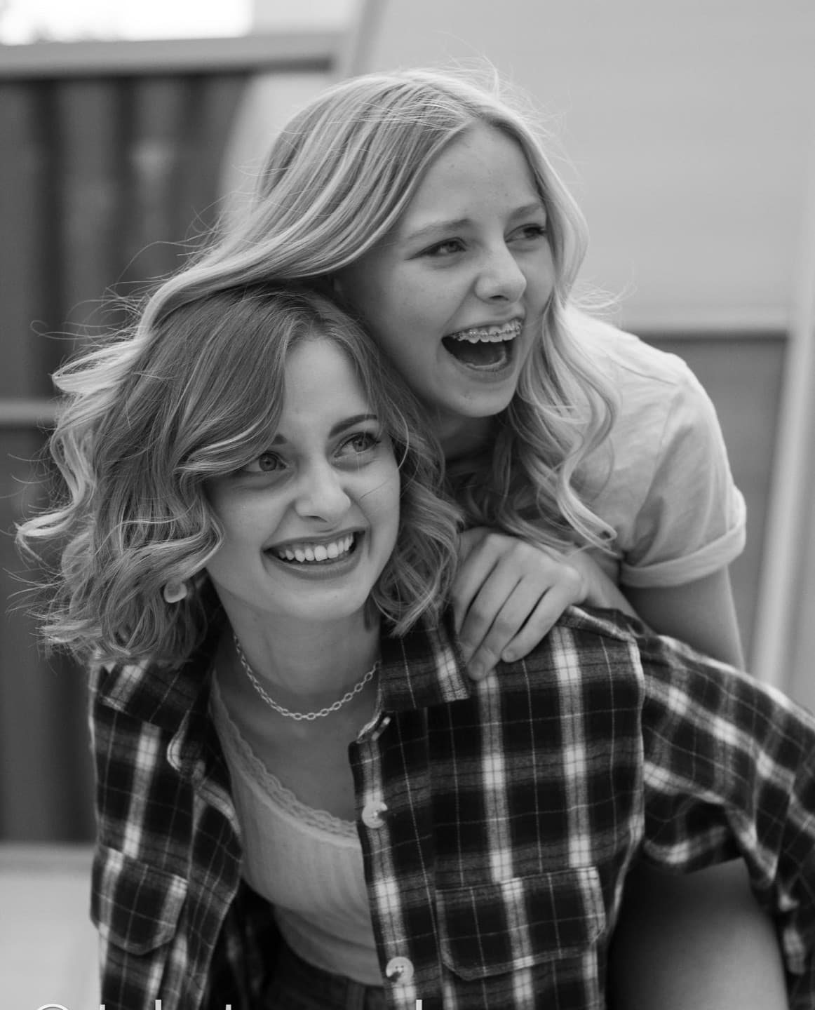 Two sisters laughing, one on the other's back, in black and white
